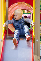 Blonde little boy sits on a childrens slide at the playground