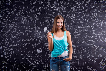 Thinking girl holding head against big blackboard, back view