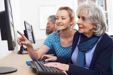 Tutor Helping Senior Woman In Computer Class - obrazy, fototapety, plakaty