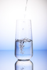 Water pouring into half-filled drinking glass