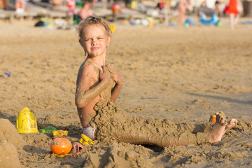 Six-year girl daubed themselves with wet sand on the beach with a sour face
