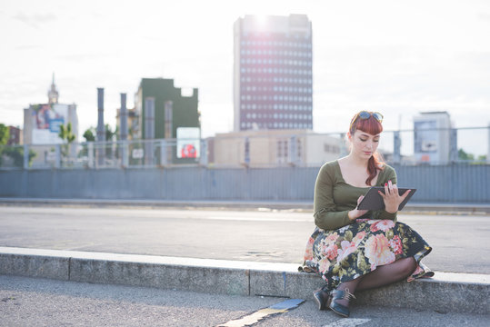 Young beautiful pin up redhead woman sitting on a sidewalk in th