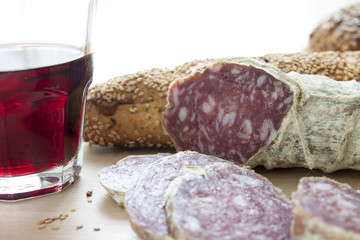 Salame casereccio a fette con pane integrale e bicchiere di vetro di vino rosso