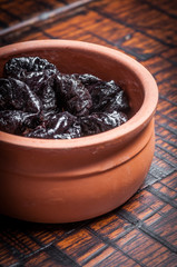 Dried plums in clay bowl on rustic wooden background