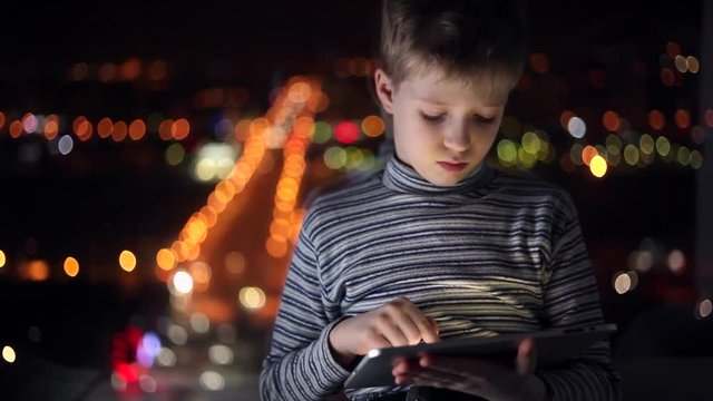 Boy playing on a tablet/A boy sitting on a background of a large window with a tablet in his hands
