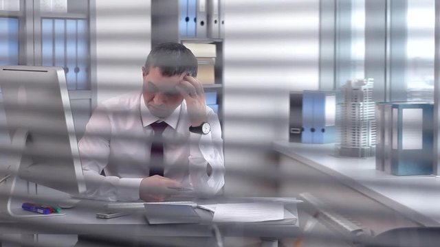 Businessman Solving Complex Business Problems/In the office behind a glass partition, we see a businessman reflecting on solving complex business problems