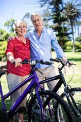 Senior couple standing with bicycle in park