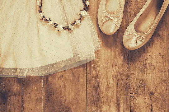 vintage chiffon girl's dress, floral tiara next to ballet shoes on wooden background. vintage filtered, sepia style image
