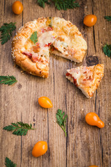 Pizza, cherry tomatoes and fresh carrot leafs on the wooden background