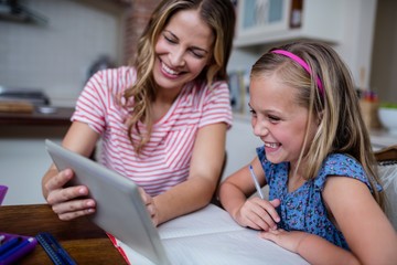 Mother using tablet while helping daughter with her homework