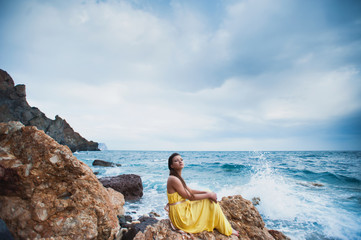 Fototapeta na wymiar A girl sits on a rock on the beach against the sky and the sea, lifestyle, recreation, solitude, meditation