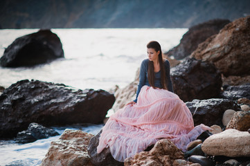 A girl sits on a rock on the beach against the sky and the sea, lifestyle, recreation, solitude, meditation