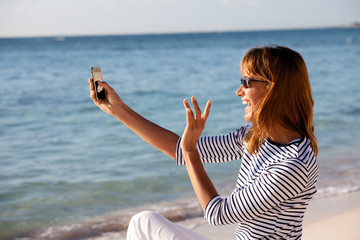Fototapeta na wymiar femme assise à la plage faisant un selfie au téléphone