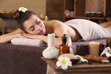 Obraz na płótnie Canvas Beautiful young girl with towel lying on massage table and aromatic candles with salt in spa salon