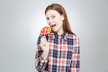 Happy teenage girl in plaid shirt standing and eating lollipop