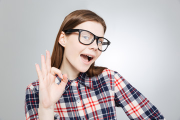 Happy charming teenage girl in glasses showing ok sign