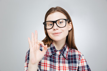 Smiling pretty teenage girl in glasses showing ok sign