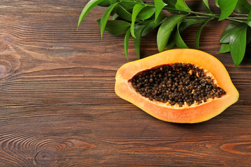Halved papaya with leaves on wooden background