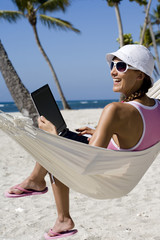 femme souriant dans un hamac à la plage avec un ordinateur portable