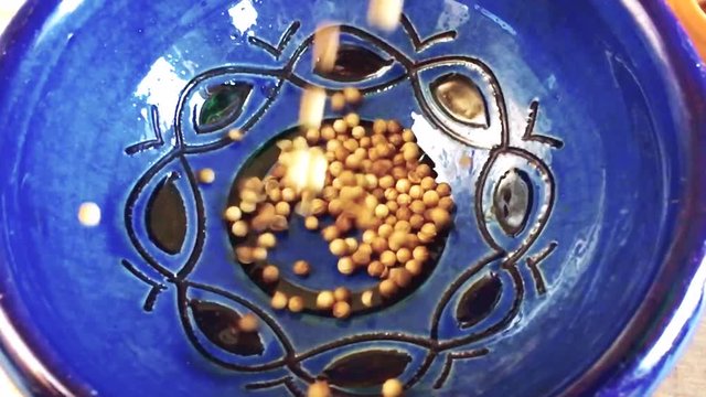 Coriander seeds being dropped into a bowl