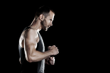 muscular man,  clasps hands in  fist, black background, place for text on the right