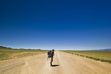 Obraz premium traveller with backpack on a lonely road in desert