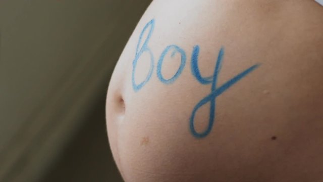 Young pregnant woman wrote on his stomach the word boy. Blue paint. Slow motion