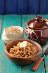 Wholegrain spelt porridge with butter in wooden bowl and raw spelt