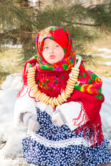 Child girl in Russian pavloposadskie folk scarf on head with floral print and with  bunch of bagels on background of snow. Portrait of girl dressed in Russian style