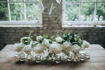 white peonies are in glass bottles next to the candles on vintage wooden table in the loft