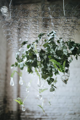 Composition of greens and glass bulbs hanging on a metal spring in the loft with a large window overlooking the garden