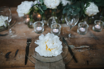 white peonies are in glass bottles next to the candles on vintage wooden table in the loft