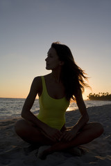 Fototapeta na wymiar femme assise en contre jour au coucher du soleil à la plage