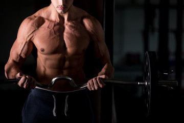 Fototapeta na wymiar Muscular man lifting a barbell in gym