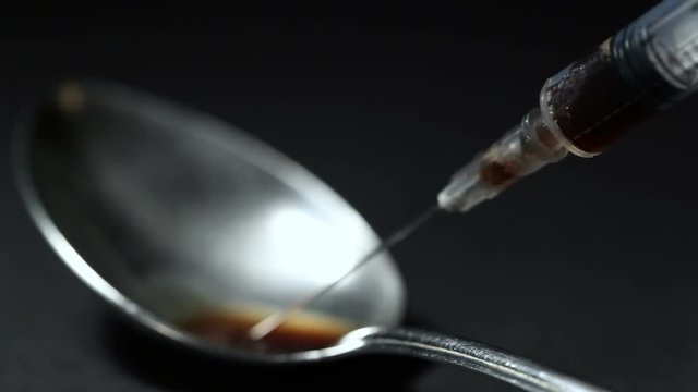 The spoon is poured with a syringe drug. Black background. Close-up