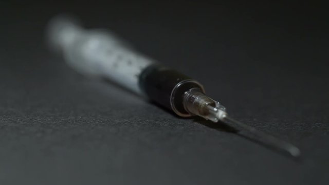 A syringe with a dose of a drug lies on a black table. Close-up. Dolly shot