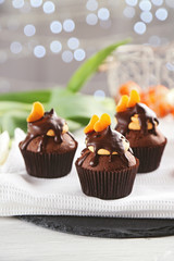 Three tasty cupcakes with slice of mandarin and chocolate on a napkin, close up