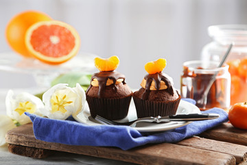 Two tasty cupcakes with slice of mandarin and chocolate on a plate, close up