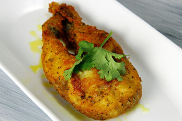 A plate of a steak of fish fried in an Indian style marinated with herbs, spices, chickpea flour and semolina flour on a wooden bakground with copy space.