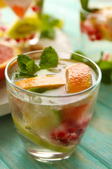 Refreshing cocktail with ice, mint, pomegranate seeds and slices of fruits on blue wooden background