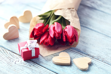 Red tulips bouquet in a paper bag with a gift box on a light-blue table