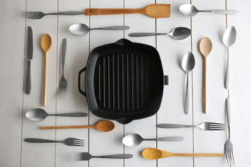 Grill pan and cutlery on white table, top view