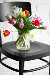 Bouquet of beautiful colorful tulips on wooden chair against white brick wall background