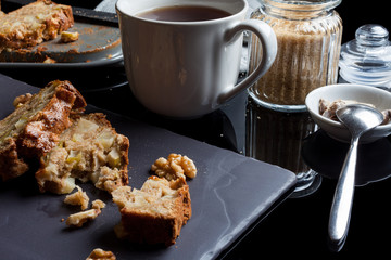 Two pieces of apple cake on black flat plate and mug with tea, sugar basin, tea time table from side