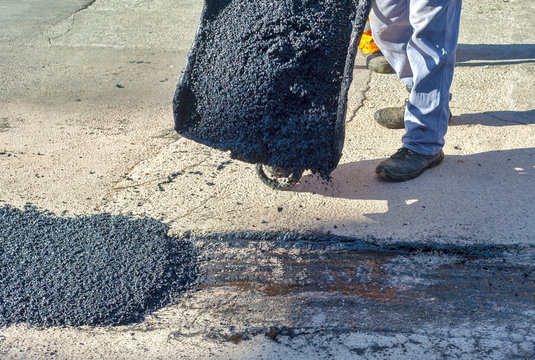 Worker empties a wheelbarrow containing asphalt during repair of a city street