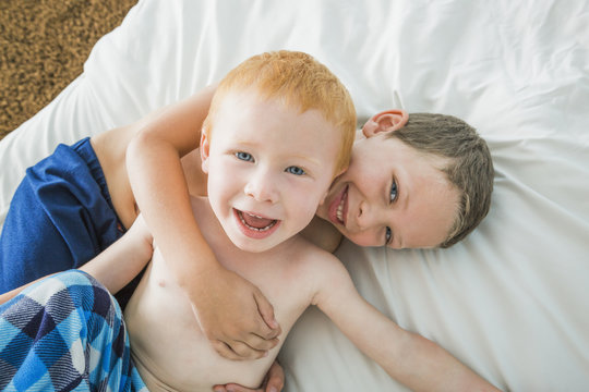 Caucasian brothers hugging on bed