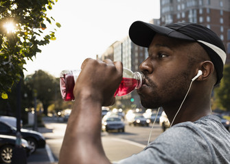 Black runner drinking juice in city