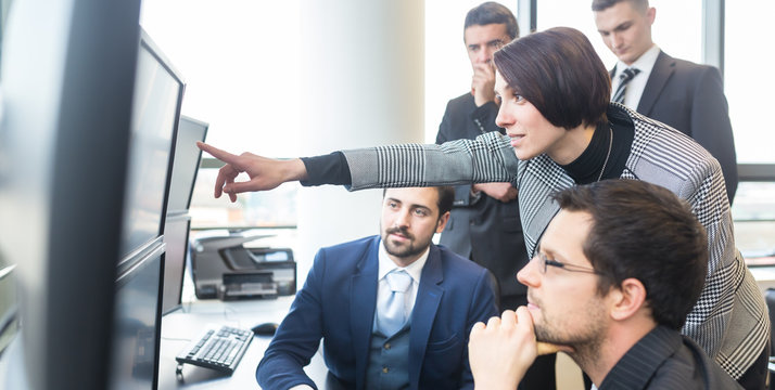 Business Team Looking At Data On Multiple Computer Screens In Corporate Office. Businesswoman Pointing On Screen. Business People Trading Online. Business, Entrepreneurship And Team Work Concept.