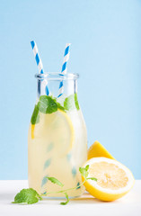 Bottle of homemade lemonade with mint, ice, lemons, paper straws and pastel blue background