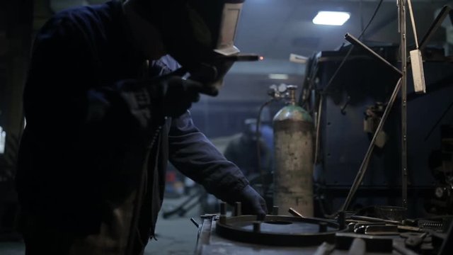 Welder in a protective helmet working on an industrial enterprise
